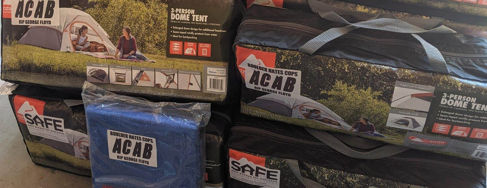 Packaged tents stacked on top of each other with ACAB stickers on them.