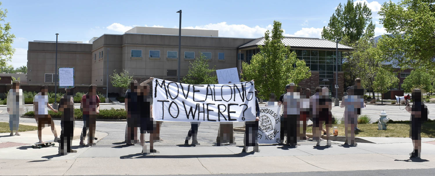 A group of 20 protesters holding a banner that reads "Move Along To Where?"